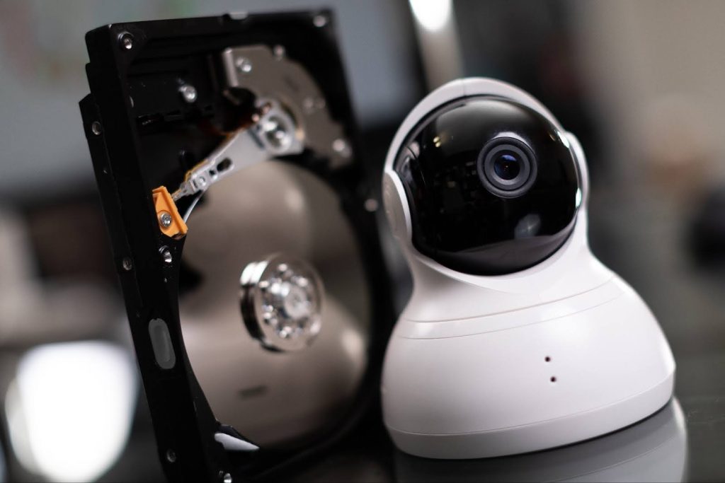 A white CCTV security camera sits next to an open hard drive, illustrating local storage solutions for surveillance footage