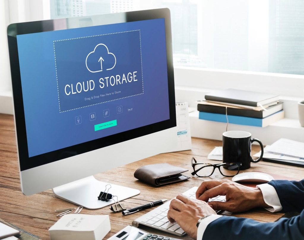 A person uses a desktop computer displaying a "Cloud Storage" interface with an upload icon